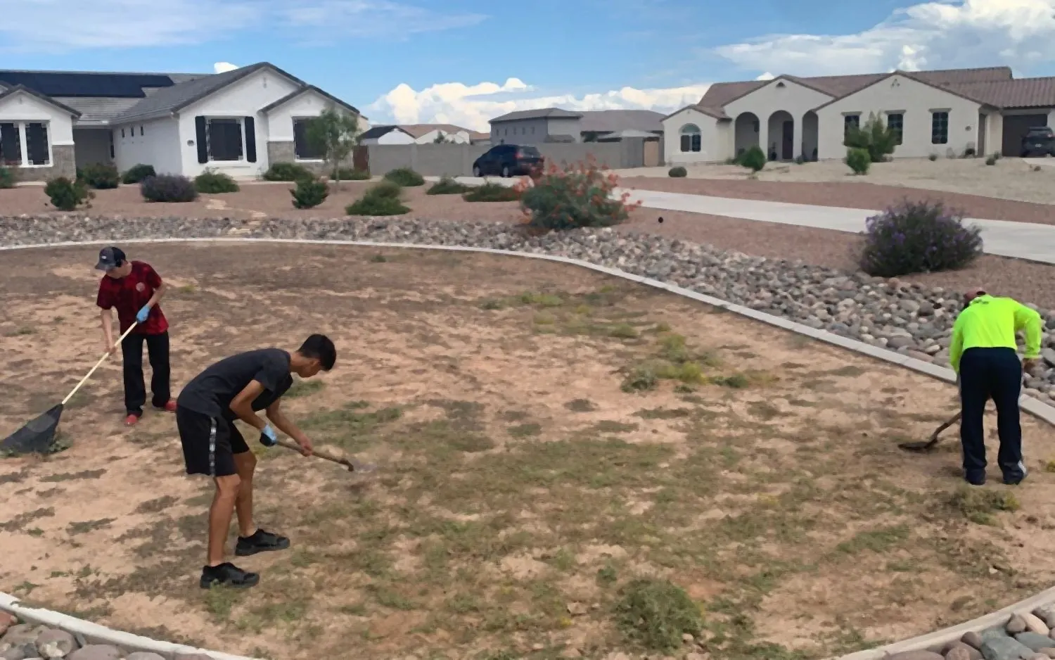 Community common area before: patchy dirt inside a river-rock border, crew at work