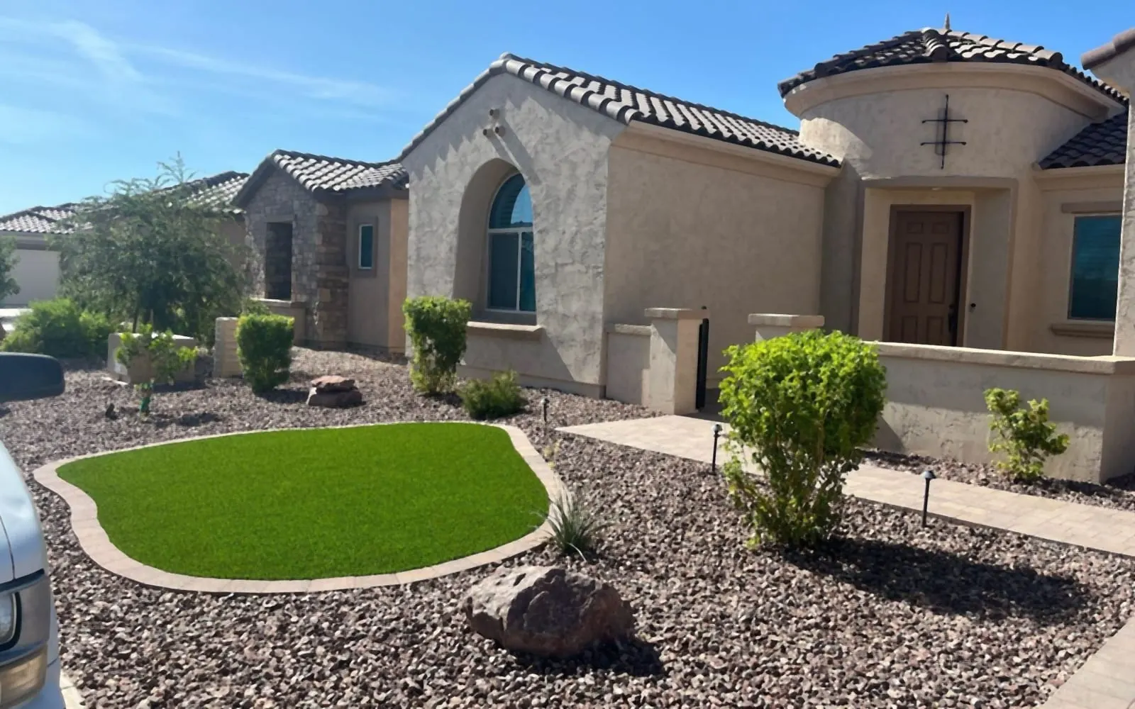 Front yard with an artificial turf oval, paver edging, rock and shrubs